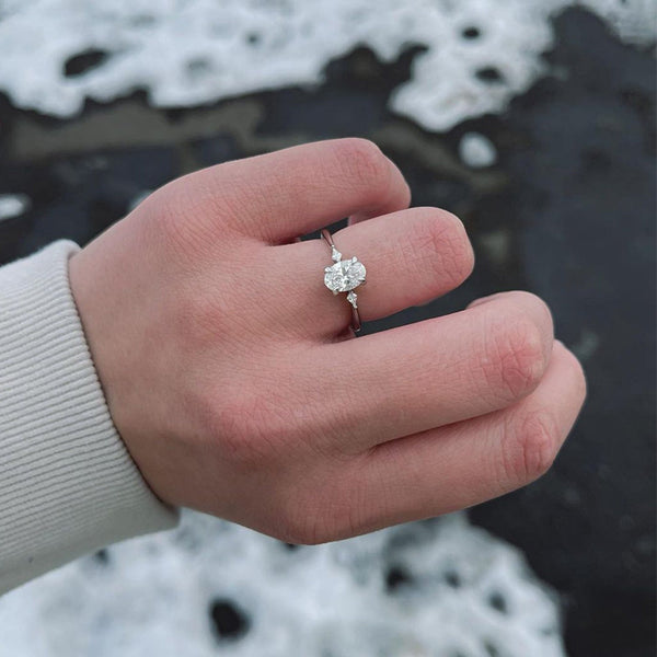 An icy-sleek three-stone ring crowned with a dazzling oval diamond that gleams like winter sunlight.
