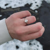 An icy-sleek three-stone ring crowned with a dazzling oval diamond that gleams like winter sunlight.