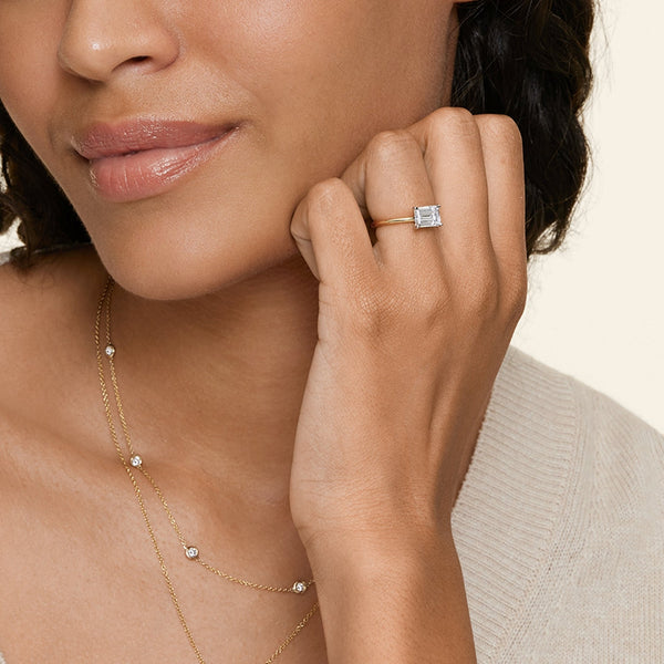 Solstice Grace is a minimalist masterpiece, showcasing an emerald-cut diamond in a classic four-prong setting with a smooth, polished band that radiates refined simplicity.